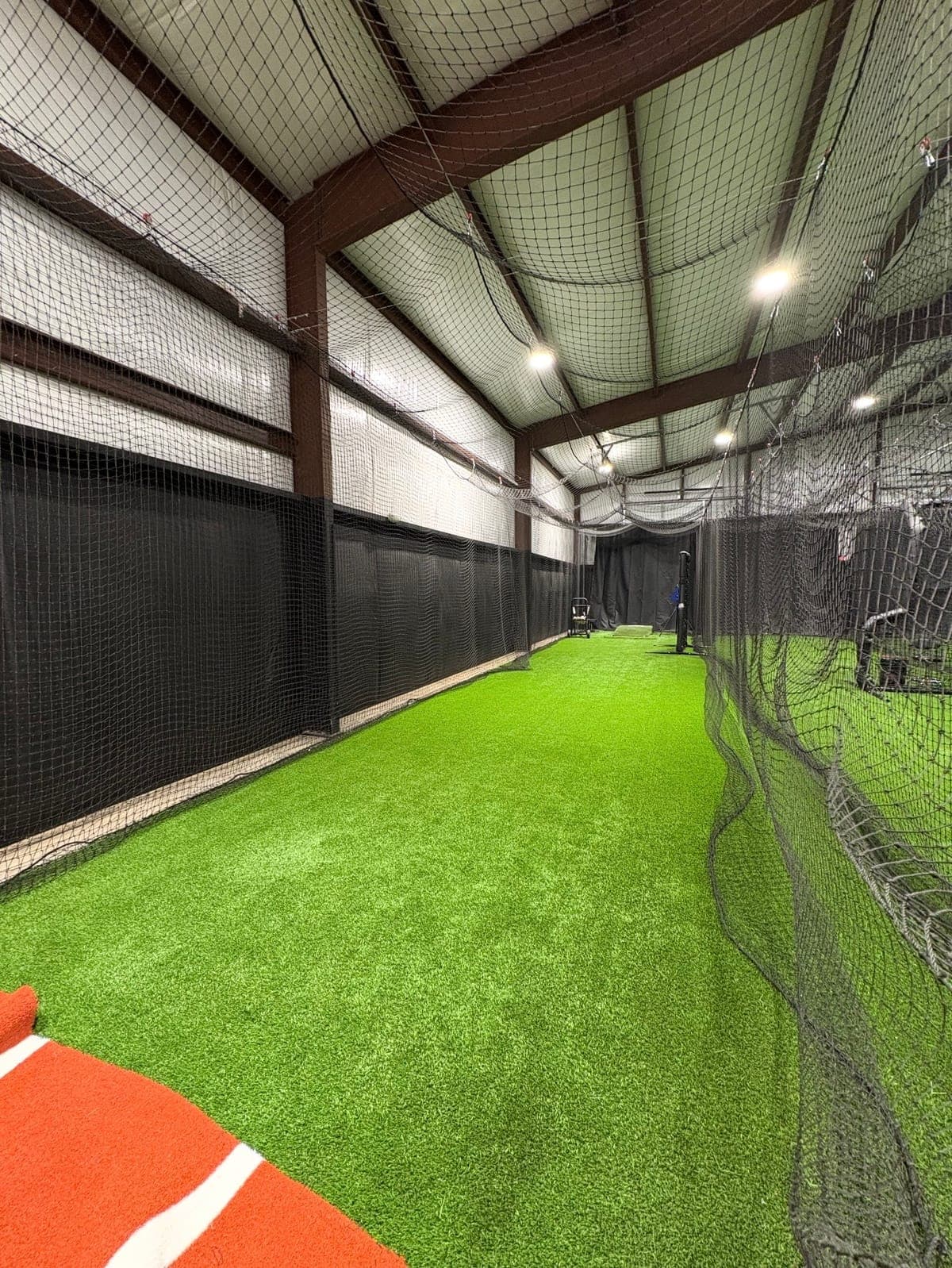 Indoor batting cage tunnel where hitters take repetitions on turf